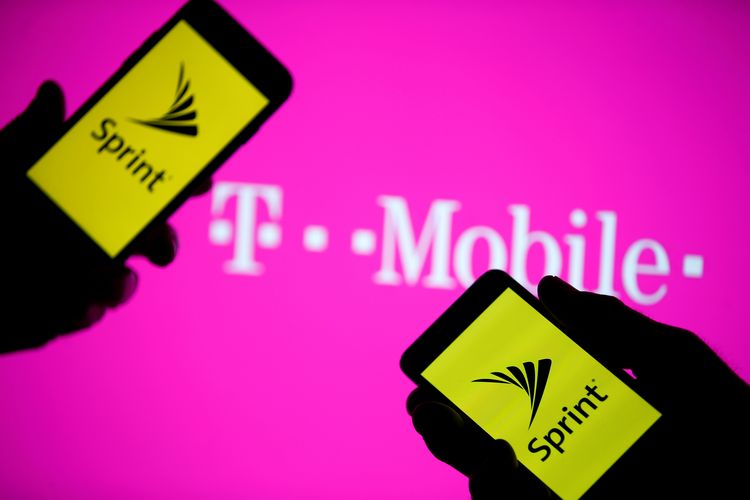 A smartphones with Sprint logo are seen in front of a screen projection of T-mobile logo
