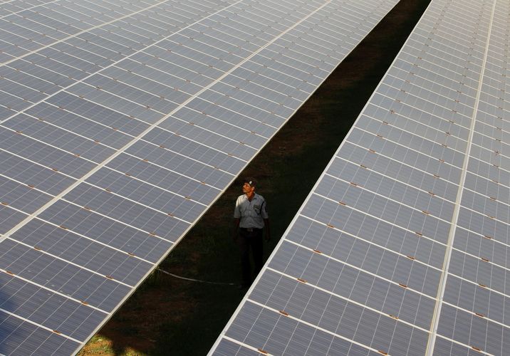 A private security guard walks between rows of photovoltaic solar panels 