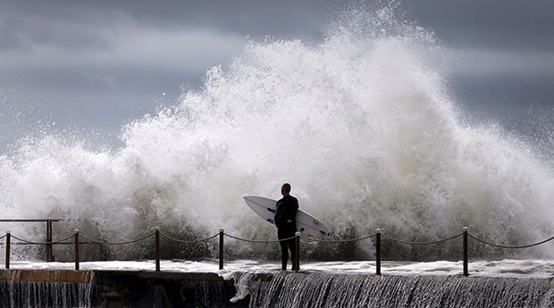 A surfer waits for a break in crashing waves before diving in for a surf off Sydney’s Collaroy Beach