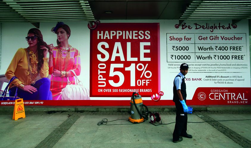 A member of the cleaning staff walks outside a department store advertising a sale at a shopping mall in Mumbai