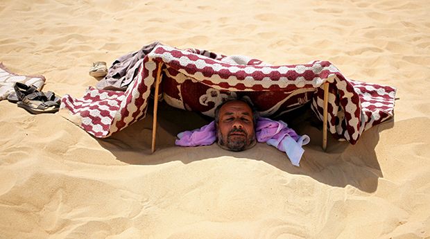 A patient buried in the hot sand looks out from under a shade