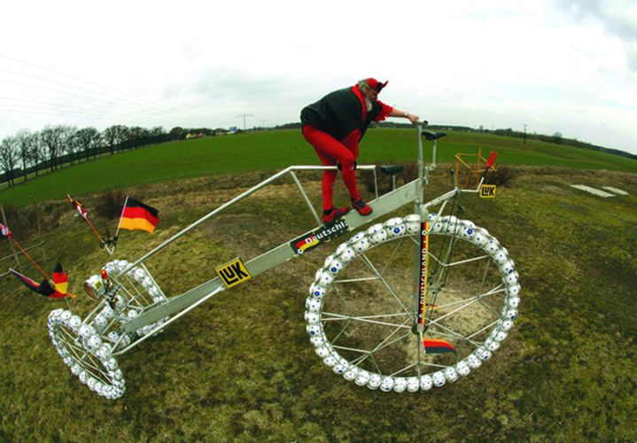 Cycling fan El Diablo climbs on his giant “soccer bicycle” in Storkow. REUTERS/Pawel Kopczynski