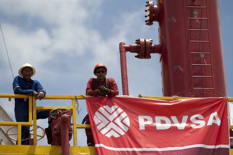 Workers stand in front of a drilling rig at an oil well operated by PDVSA