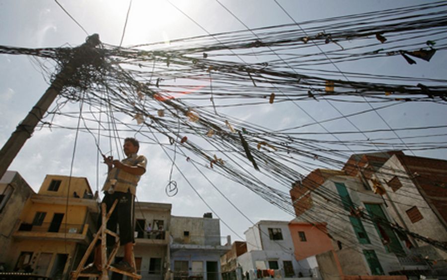 A man stands on a stepladder to fix tangled overhead electric power cables at a residential area in 