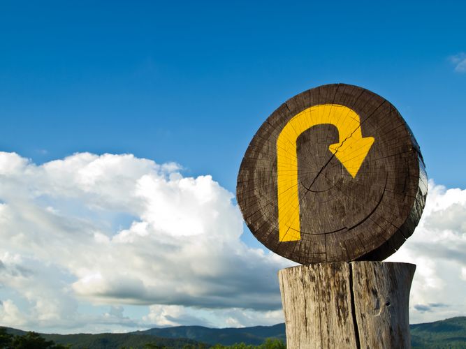 A wooden U turn sign on the top the mountain with bright sky