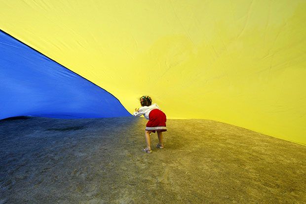 A girl walks under a giant Ukrainian national flag, held by people celebrating the Day of the State Flag, in Kiev