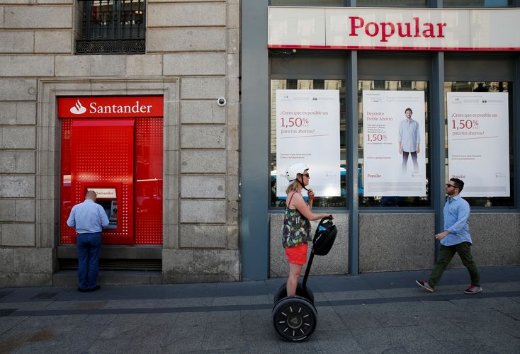 A man uses a cash dispenser at a Santander branch next to a Banco Popular branch in Madrid