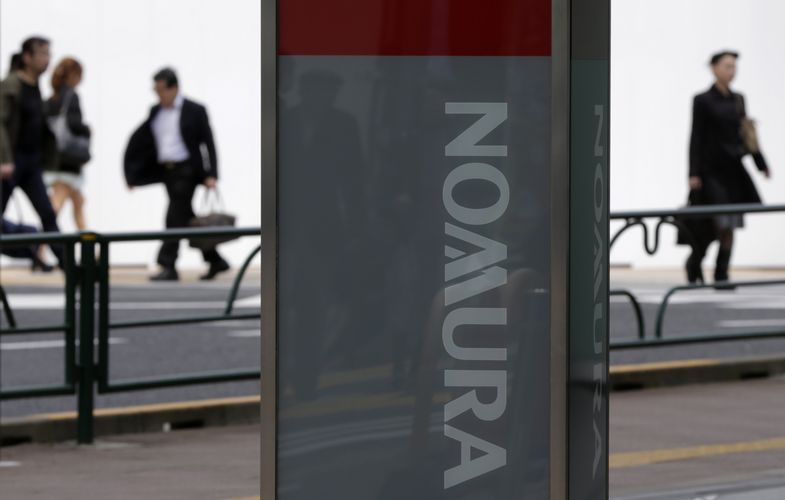 People walk behind a signboard of Nomura Securities outside its branch in Tokyo 