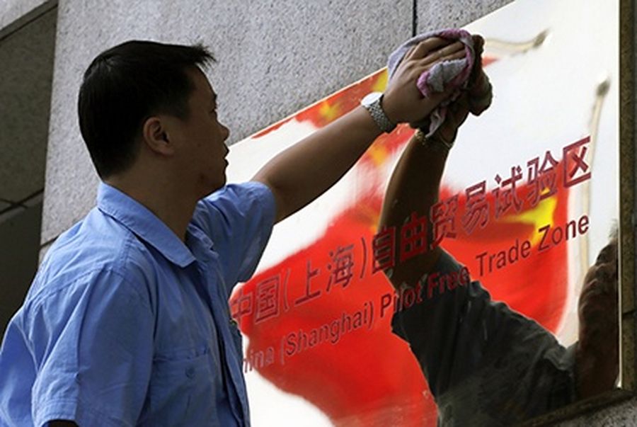 A reflection of the Chinese national flag is seen in a sign for the new China (Shanghai) Pilot Free Trade Zone, as a worker cleans it, in Shanghai.