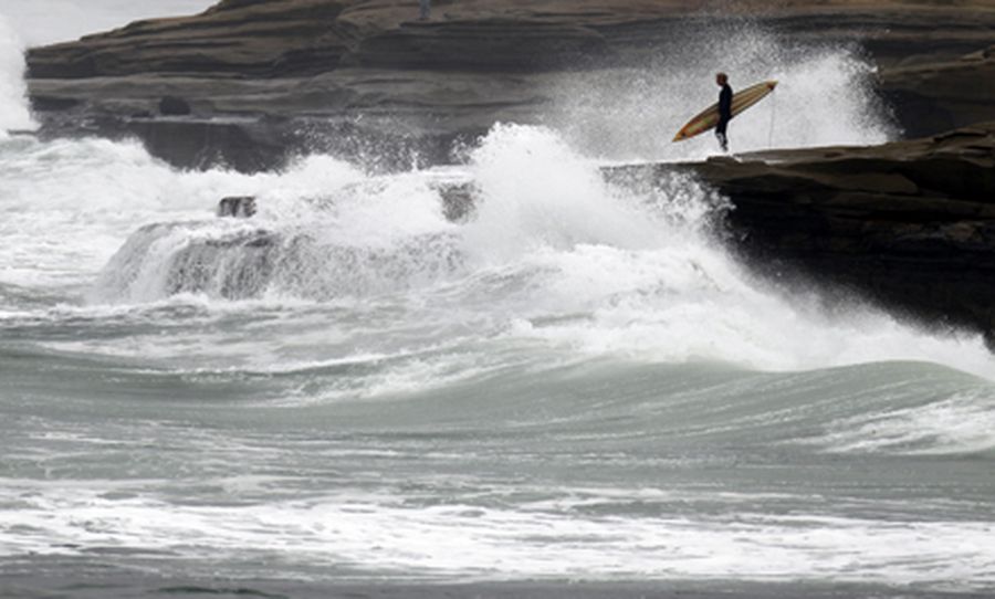 A lone surfer waits to enter the water as the coastline is hit by large surf during a winter storm i