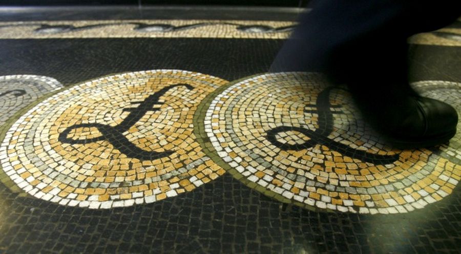 An employee is seen walking over a mosaic of pound sterling symbols set in the floor of the front hall of the Bank of England in London