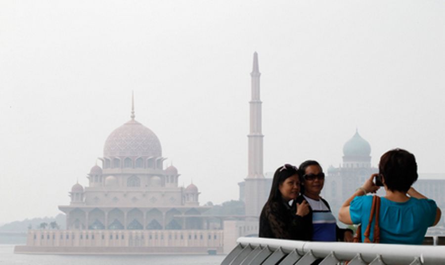 Tourists take pictures against a smog covering Malaysia's Putra Mosque and Putra Perdana in Putrajay